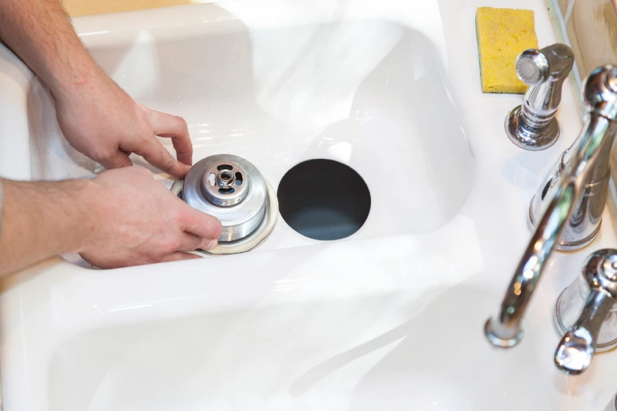 A male plumber using a drain snake to unclog kitchen sink
