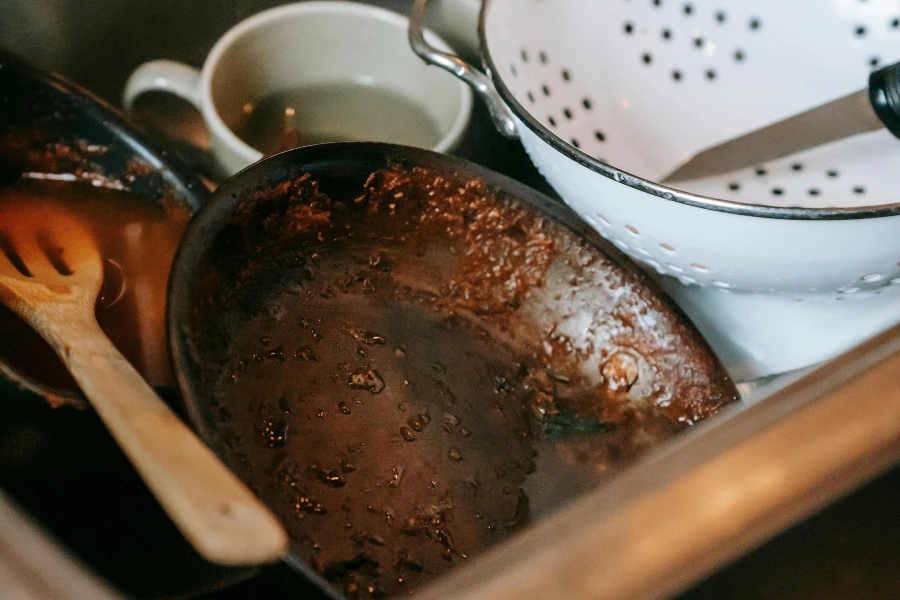 dirty pan, collander, knife, and mug in sink